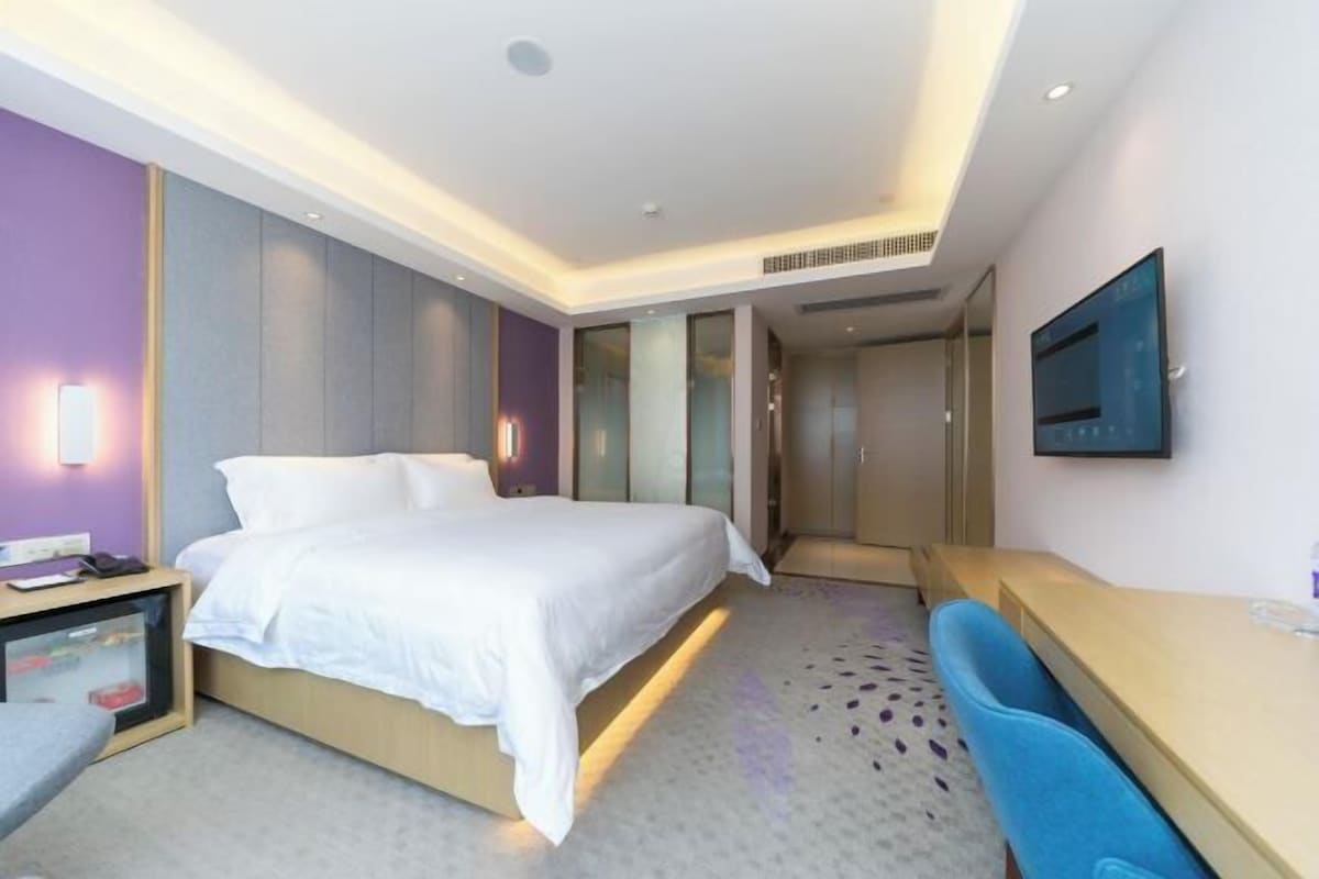 A modern hotel room with a bed, bedside table, desk, and a TV mounted on the wall.