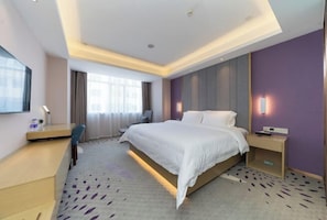 A hotel room with a bed, bedside table, desk, chair, and a large window. - Lavande Hotel (Foshan)