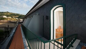 A rooftop terrace with a green railing, a view of the cityscape, and a building with a dark, textured facade.