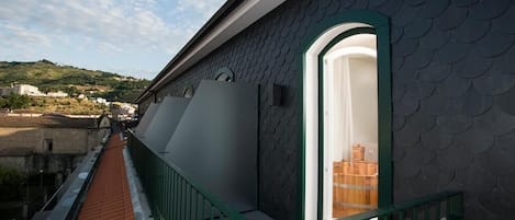 Una terraza en la azotea con barandilla verde, vista panorámica de la ciudad y un edificio con fachada oscura y texturizada.