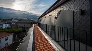 A rooftop terrace with a metal railing, a view of the cityscape, and a building with a textured facade.