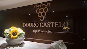 A reception desk with a logo and name of the hotel, "Douro Castelo Signature Hotel," and two flower arrangements.