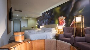 A hotel room with a bed, two armchairs, a wooden side table, a television, and a large wall mural.