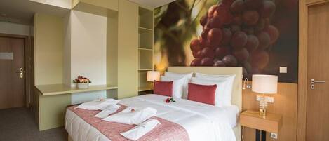 A hotel room with a large bed, a bedside table with a lamp, a wall-mounted shelf, and a door.