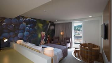 Quarto de hotel moderno com uma cama grande, área de estar com vista, banheira de madeira e vista panorâmica da cidade pela janela.