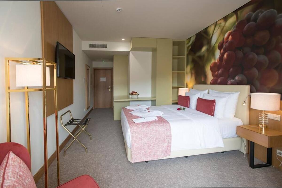 A hotel room with a bed, a TV, a desk, and a large wall mural.