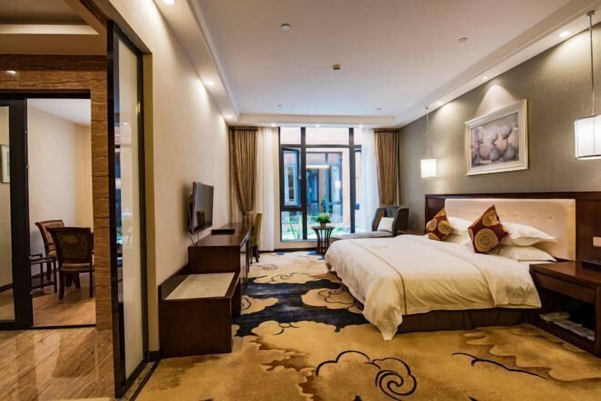 A hotel room with a large bed, a desk, a TV, and a view of the outdoors.