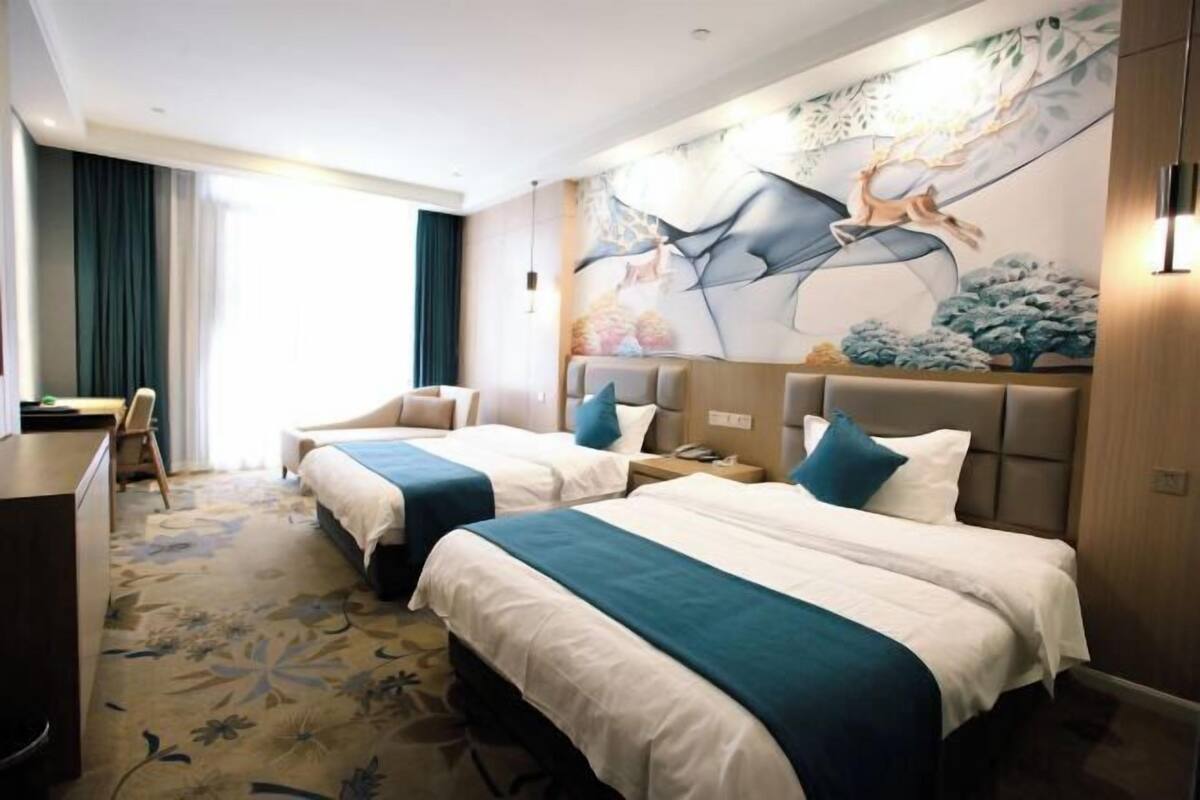 A hotel room with two beds, a desk, and a large mural on the wall.