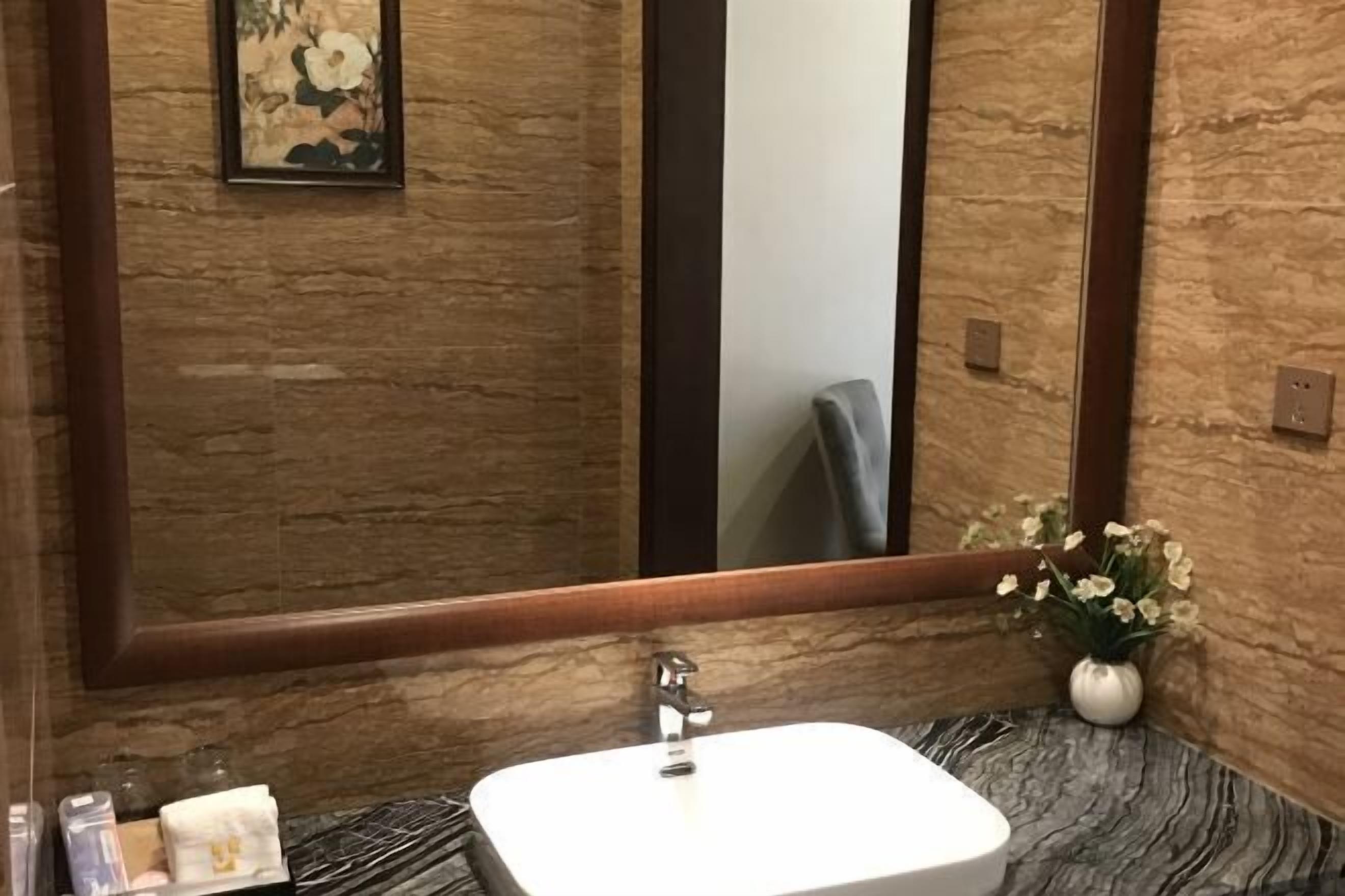Un baño con lavamanos de mármol, un espejo grande y un florero con flores.