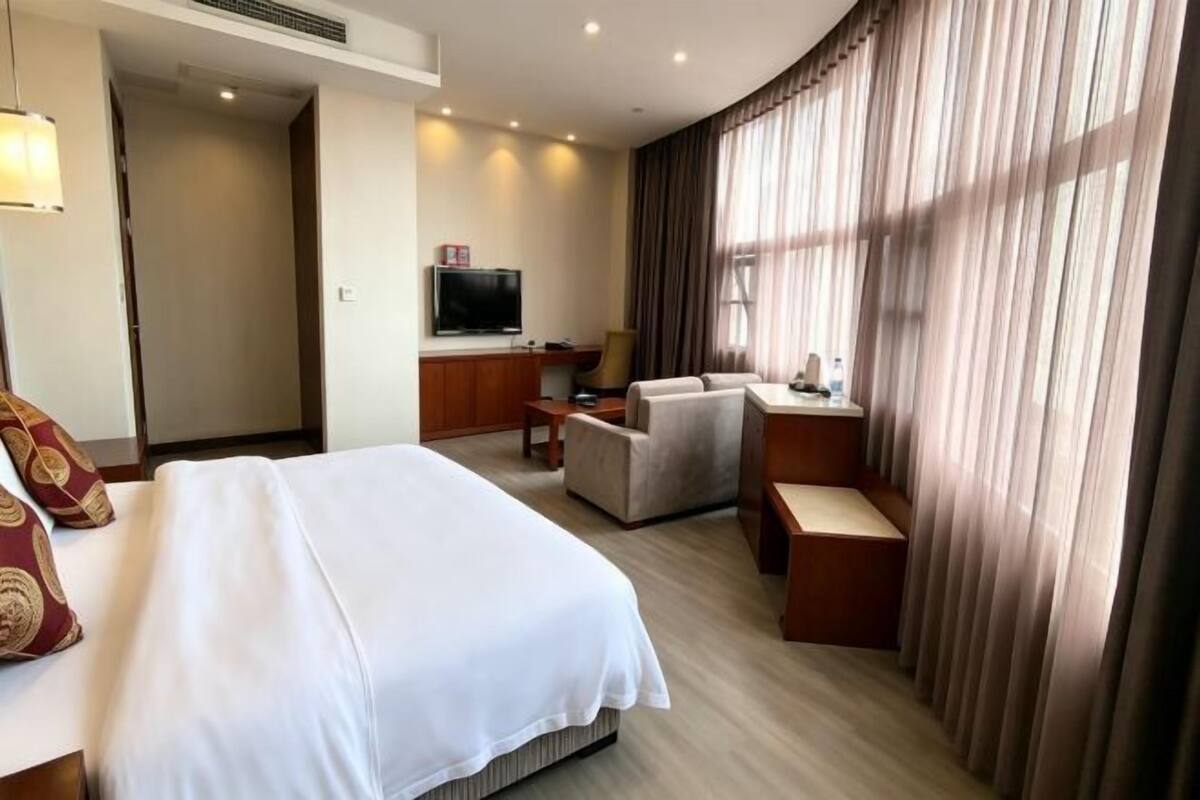 A hotel room with a bed, a desk, a chair, a television, and a large window with curtains.