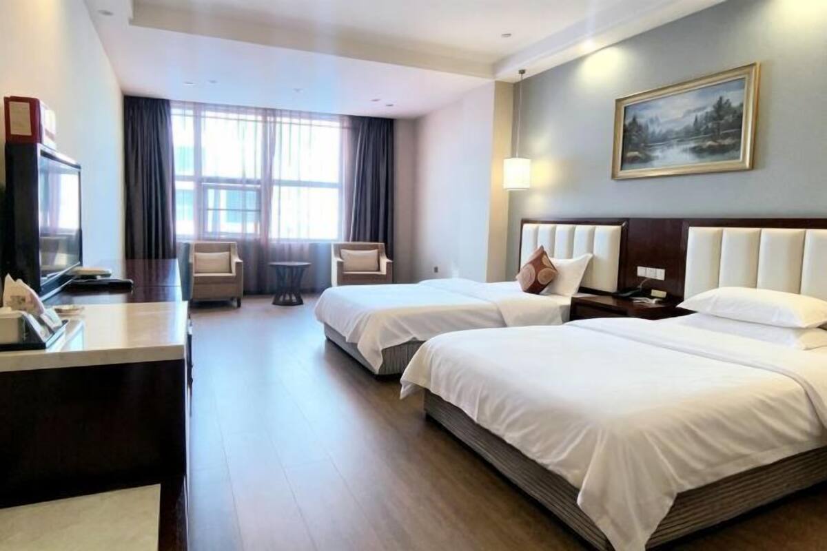 A hotel room with two beds, a desk, a chair, a TV, and a painting on the wall.