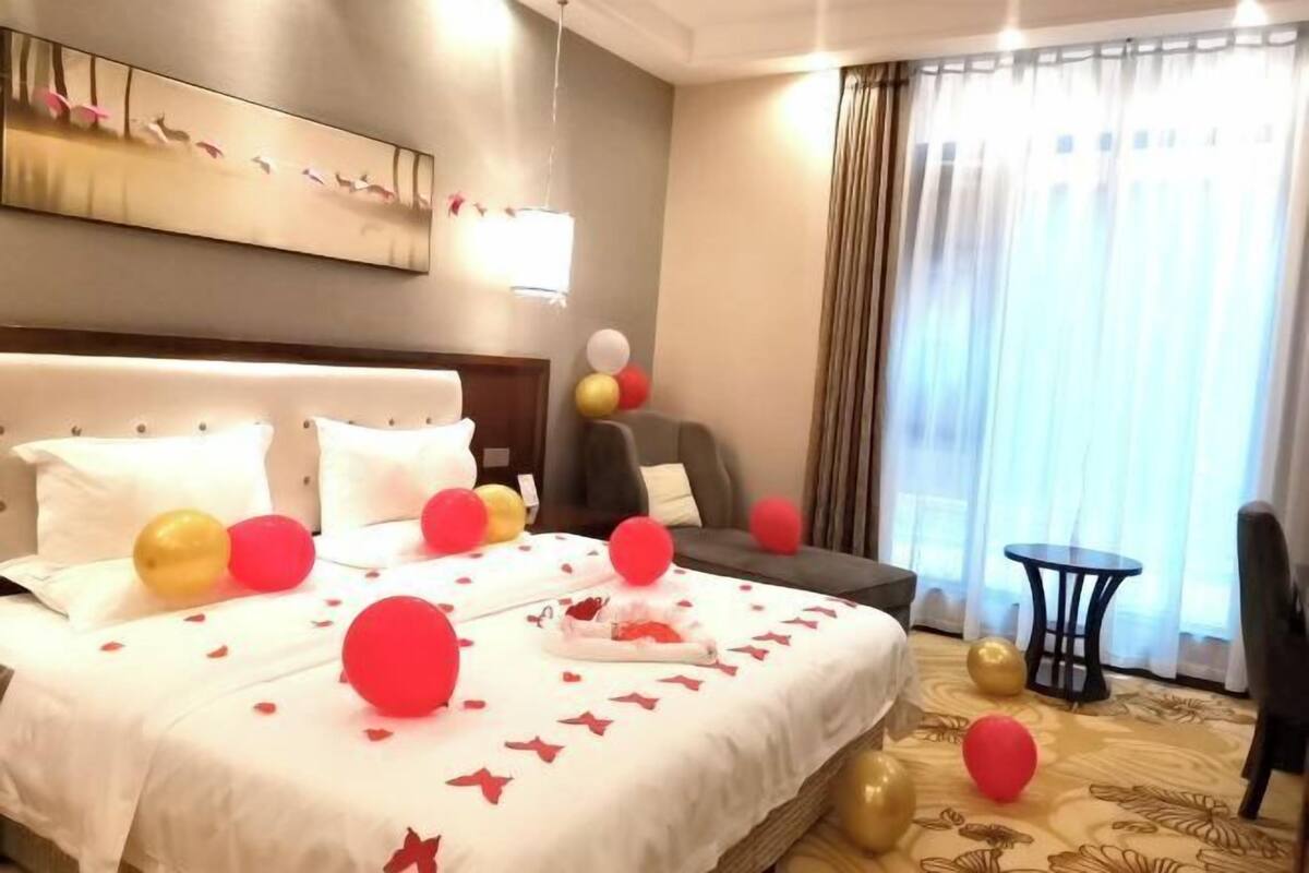 A hotel room with a bed, a chair, a small table, and a window with curtains.
