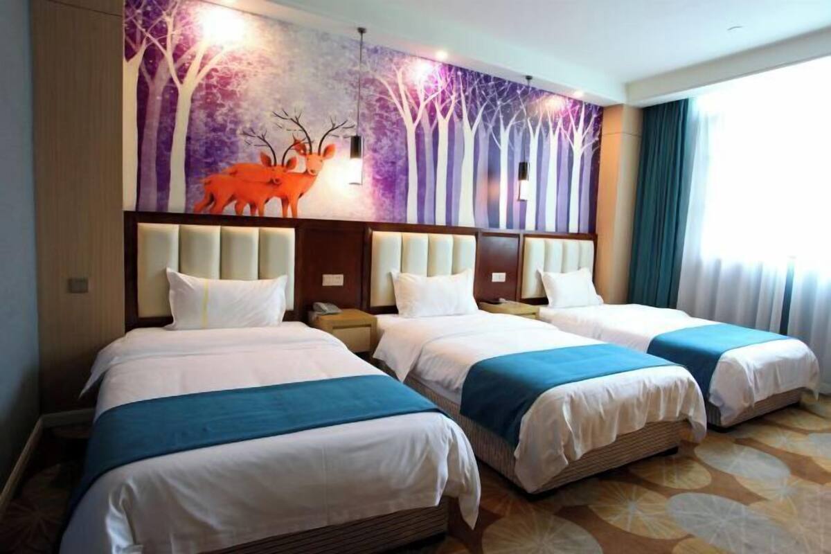 A hotel room with three beds, a mural with a deer, and a large window with curtains.