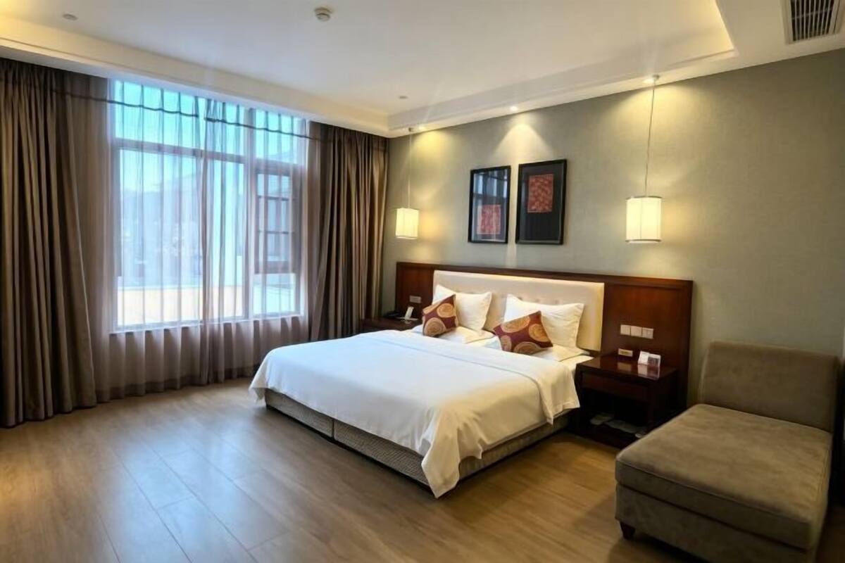 A hotel room with a large bed, a nightstand, a chair, and a window with curtains.