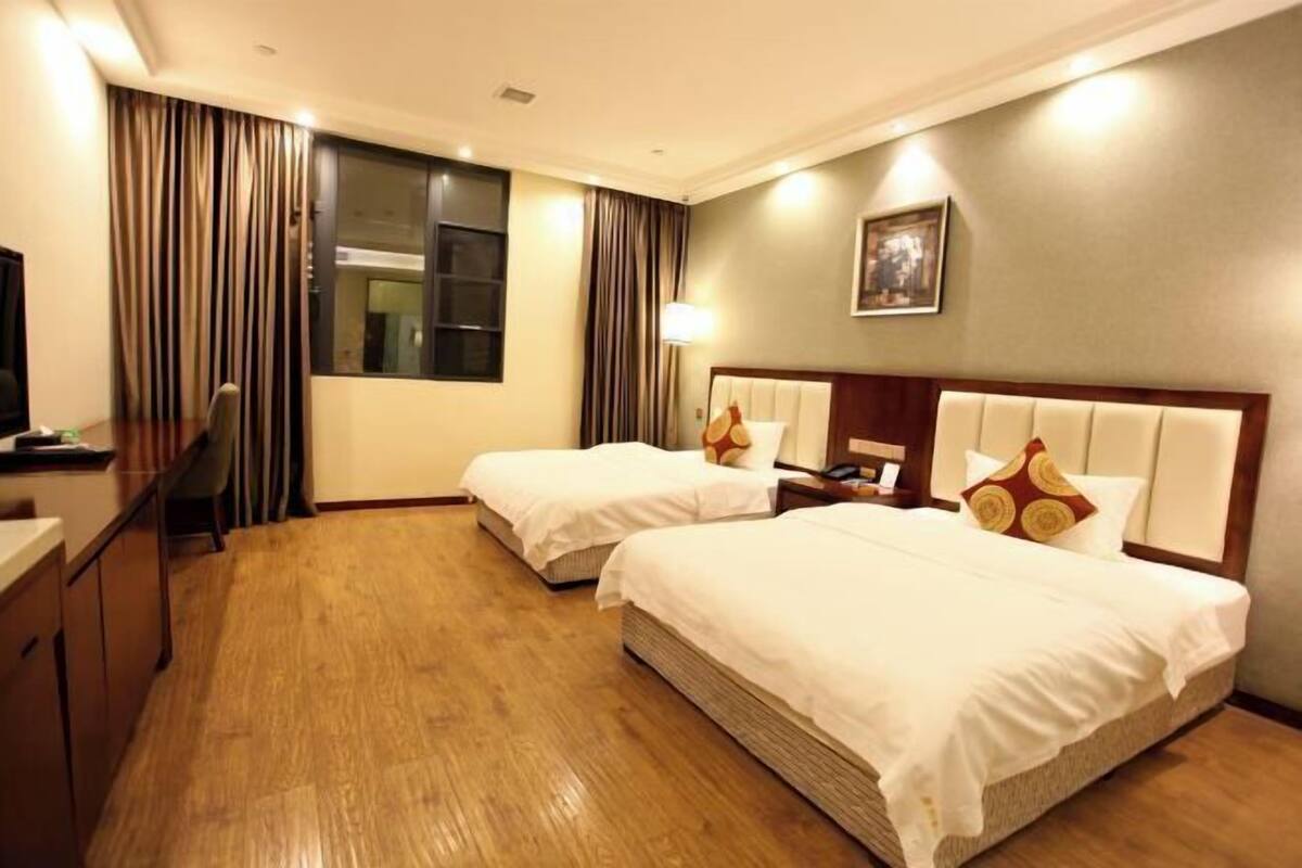 A hotel room with two beds, a desk, a chair, a television, and a window with curtains.