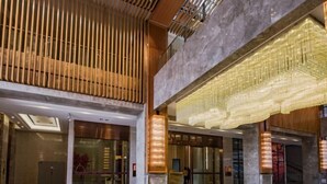 Un vestíbulo amplio con techo alto, listones de madera modernos y una gran estructura mural iluminada.
