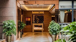 Un vestíbulo de hotel con mostrador de recepción, plantas en macetas y suelo de baldosas.