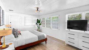 A bedroom with a bed, bedside table, lamp, TV, and a dresser.