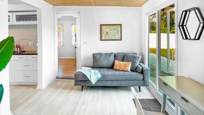 A modern living room with a grey sofa, a wooden ceiling, and a large window.