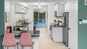 A modern kitchen with white cabinets, a central island, and pink chairs.