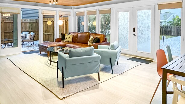 A spacious living area with a wooden ceiling, large windows, and a mix of seating arrangements including a sofa and chairs.