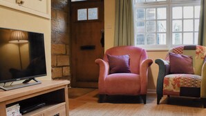 Un accogliente soggiorno con una porta in legno, una televisione su un mobiletto in legno e due poltrone con cuscini.
