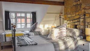 Una camera da letto con due letti, un muro in pietra, una finestra con tende e una lampada da comodino.