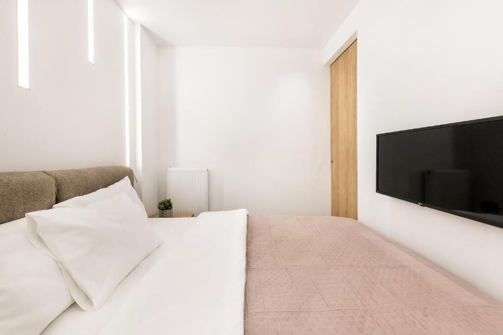 A modern bedroom with a bed, a TV mounted on the wall, and a radiator.