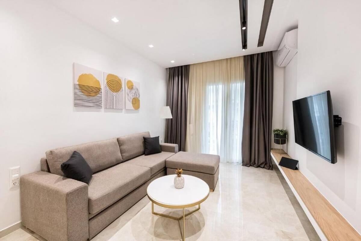 A modern living room with a beige sofa, a round coffee table, and a flat-screen TV mounted on the wall.