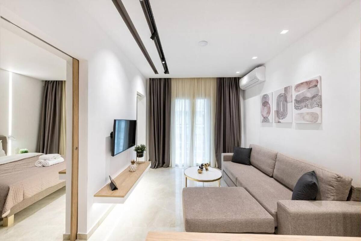 A modern hotel room with a bed, a sofa, a TV, and a small table.
