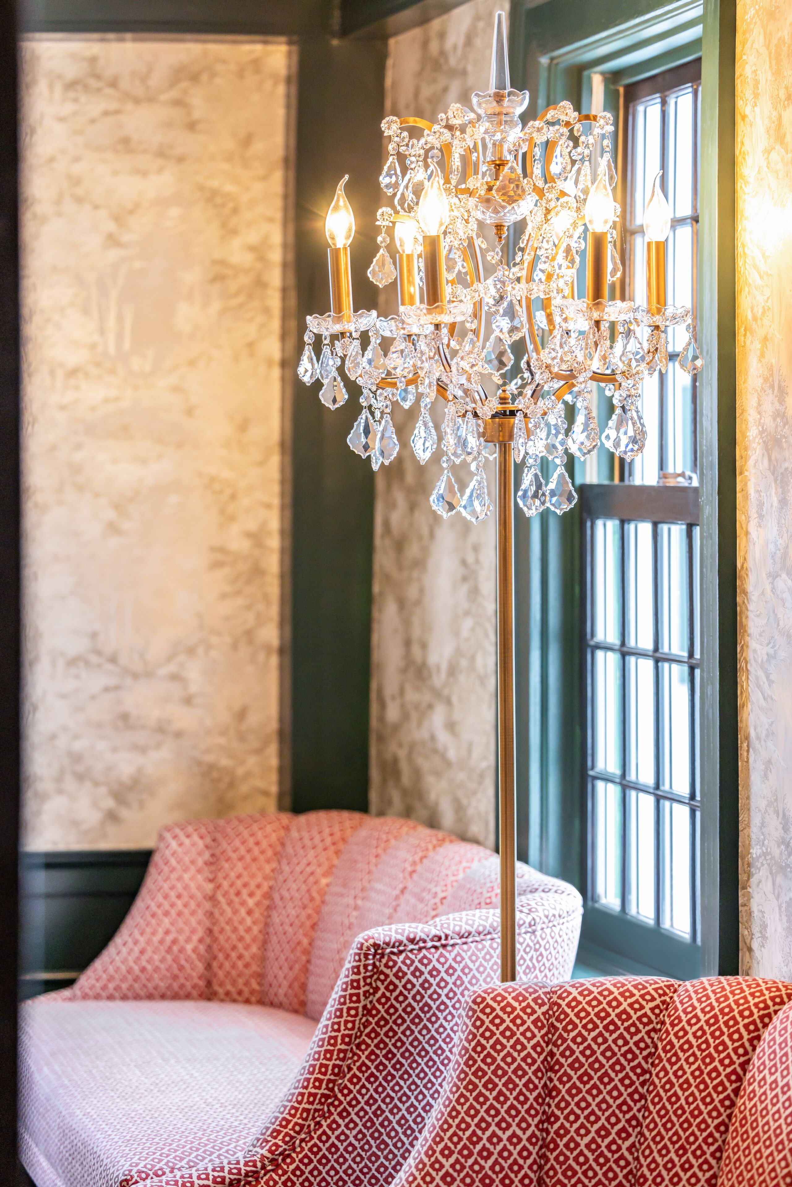 A chandelier with multiple lights and crystal decorations in a room with patterned cushions and a window with vertical bars.