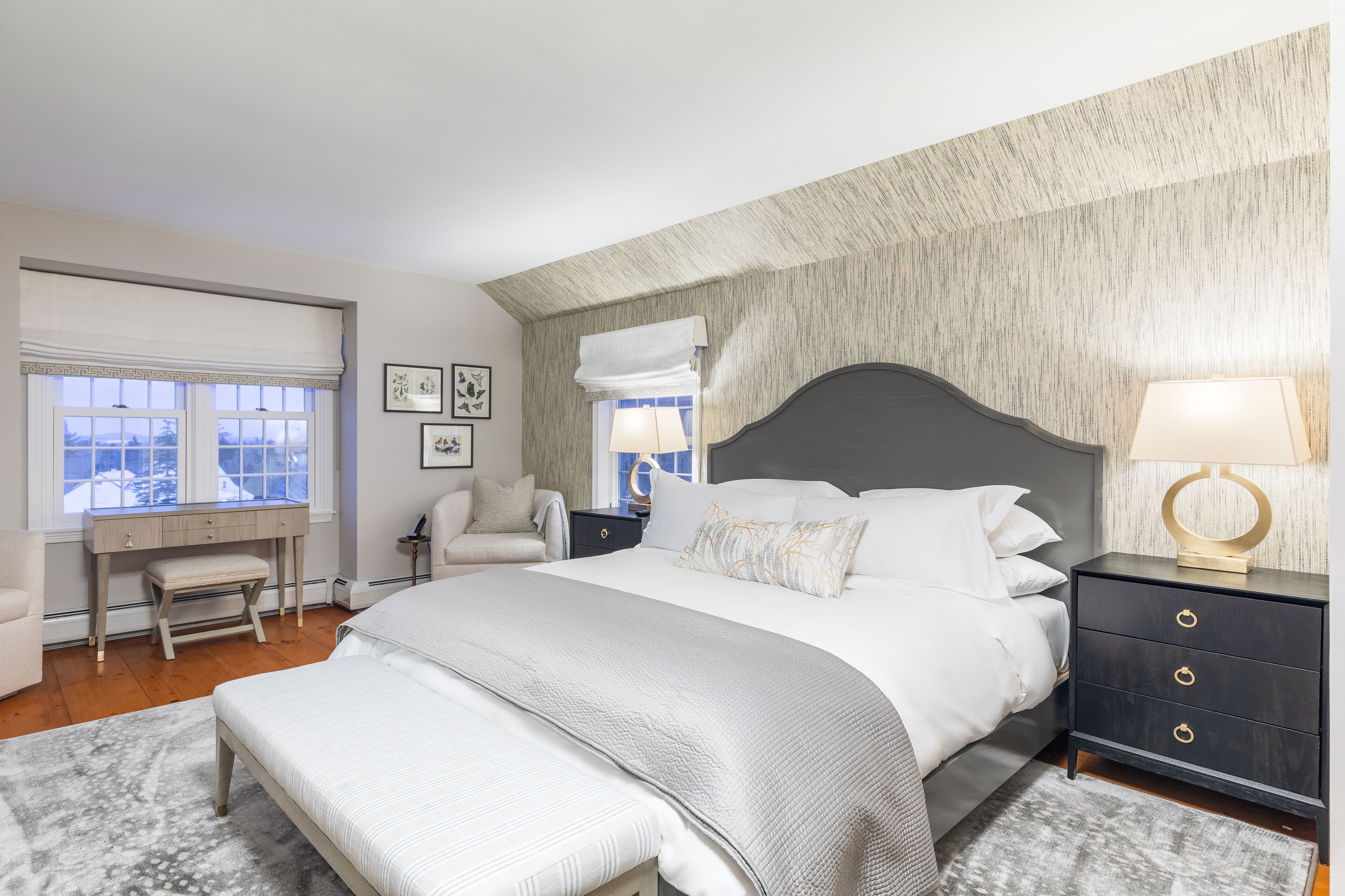 A bedroom with a large bed, a desk, a chair, and a nightstand with a lamp.