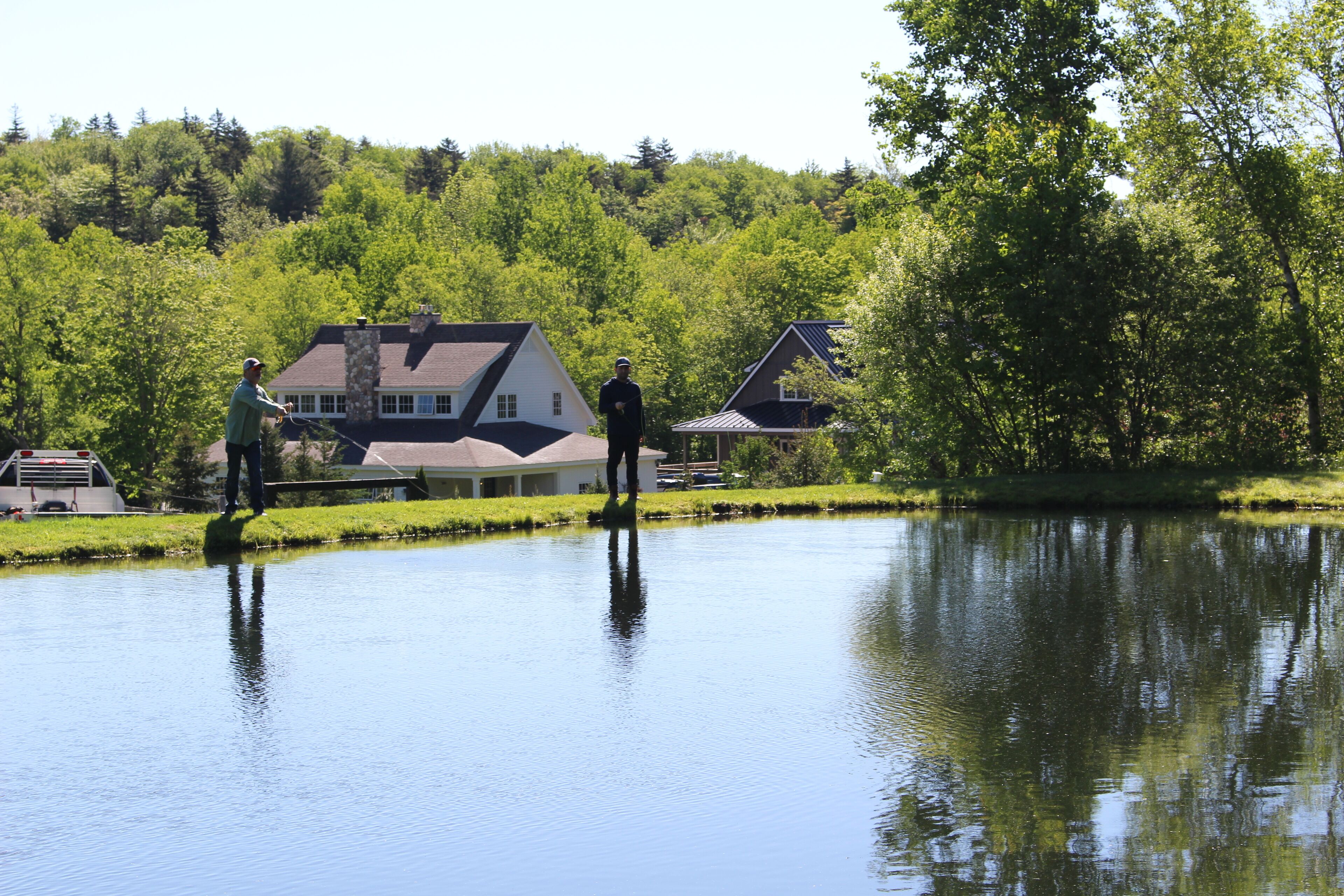 Una casa junto a un lago tranquilo, con césped y un pequeño muelle.