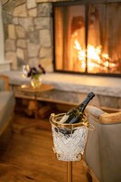 Un cuarto acogedor con pared de piedra, una chimenea y una mesa con una botella de champán en una copa de cristal.