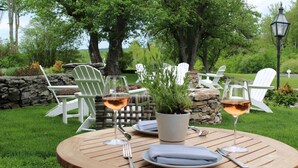 Una mesa de madera redonda al aire libre con sillas blancas, dos copas de vino y una planta en maceta.