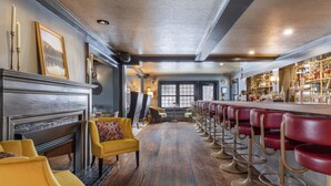 Una zona de bar con una barra alargada y varios taburetes, una chimenea con repisa, y un sillón amarillo.