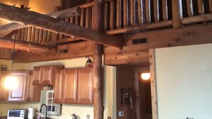 Interior rústico de una cabaña con comedor en un entrepiso, vigas de madera y ventilador de techo.