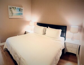 Enjoy a restful stay in this cozy room featuring a comfortable bed, a convenient nightstand with a lamp, and a beautiful beach scene.