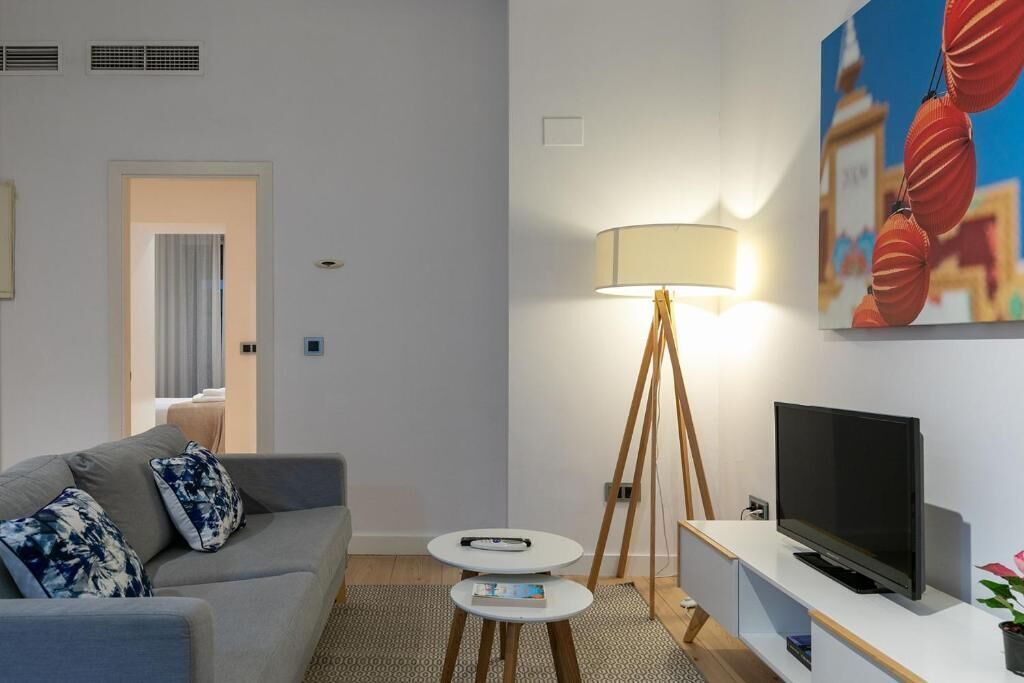 A modern living room with a grey sofa, a small round table, a floor lamp, and a flat-screen TV.