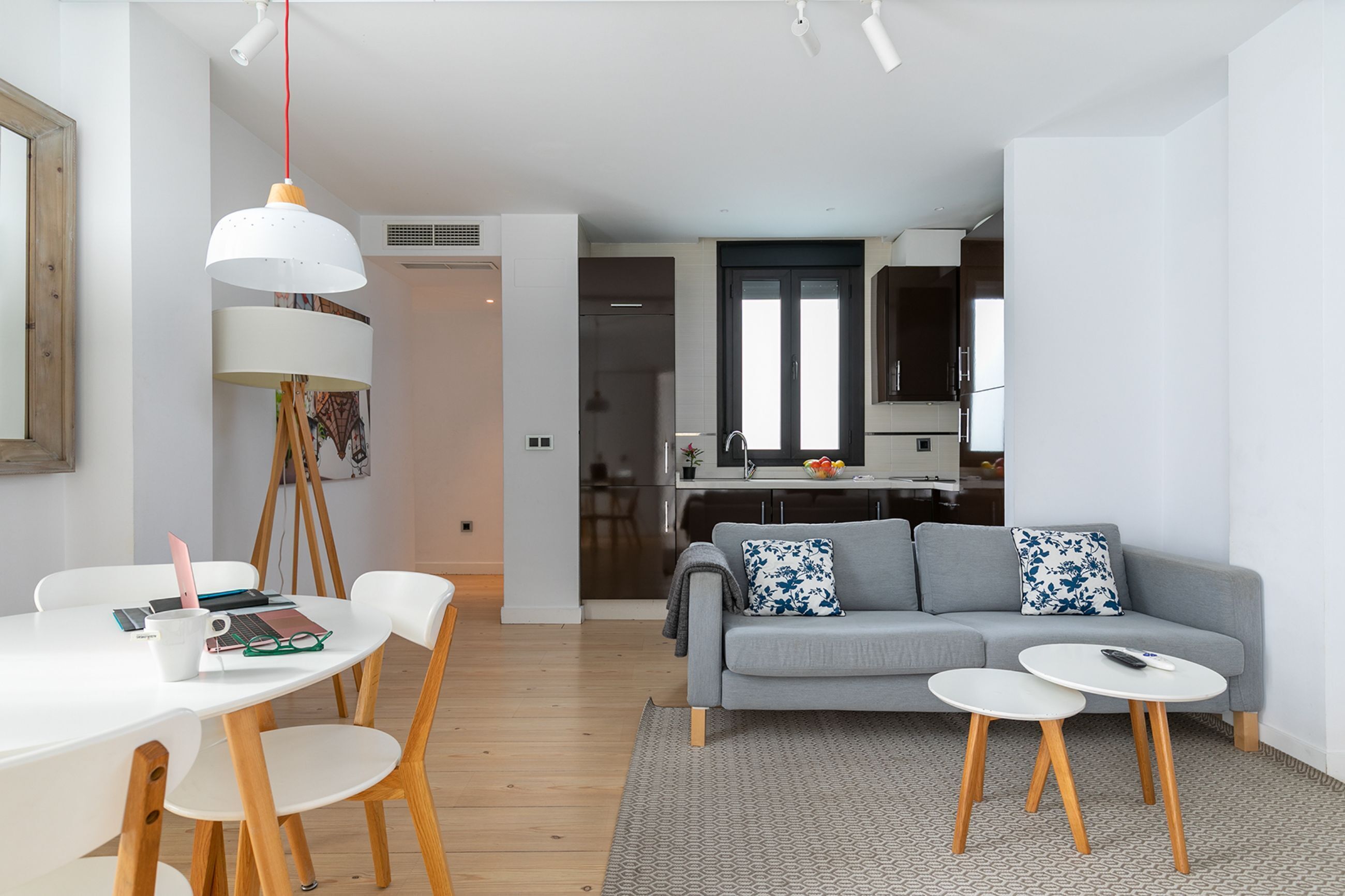 A modern living room with a grey sofa, two white coffee tables, and a dining area with a white table and chairs.