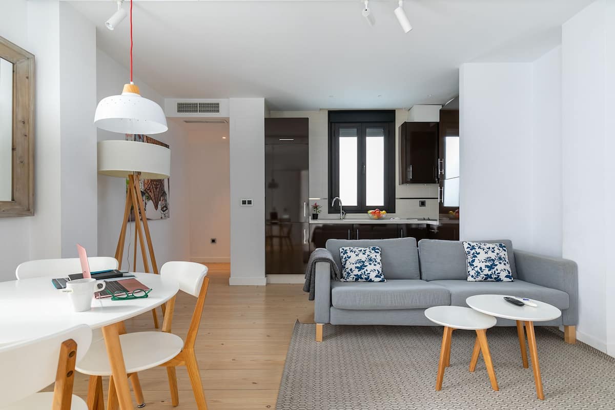 A modern living room with a grey sofa, two white coffee tables, and a dining area with a white table and chairs.