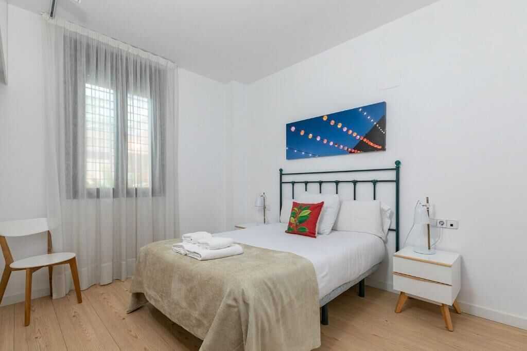 A bedroom with a bed, a nightstand, a chair, and a window with curtains.