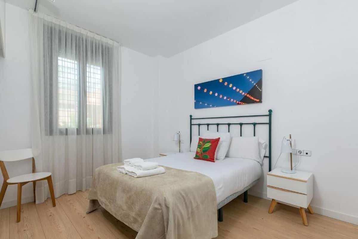 Une chambre à coucher avec un lit, une table de chevet, une chaise et une fenêtre avec des rideaux.