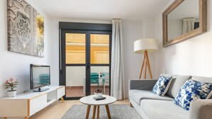 A modern living room with a grey sofa, a small round table, a TV, and a large window with curtains. - Holiday Rentals Tempa Museo (Seville)