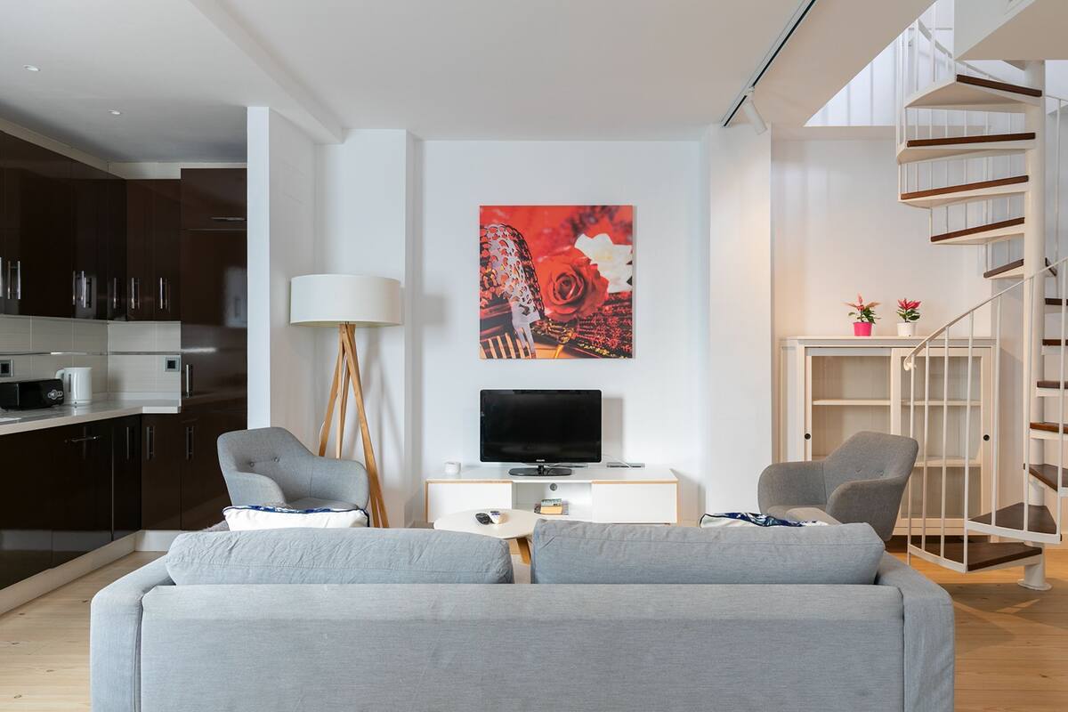 A modern living room with a grey sofa, a flat-screen TV, and a painting on the wall.