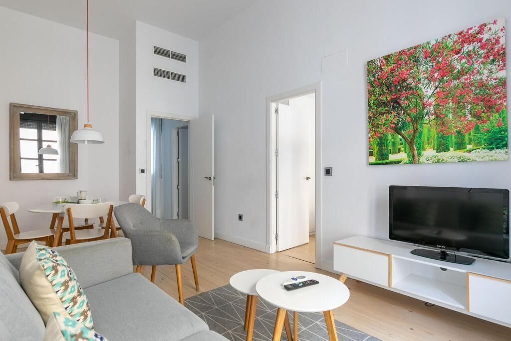 A modern living room with a sofa, chairs, a dining table, a TV, and a painting.