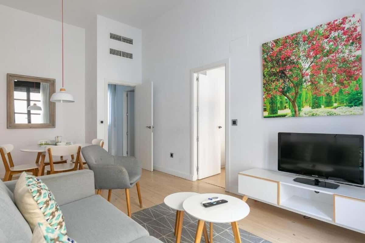 A modern living room with a sofa, chairs, a dining table, a TV, and a painting.