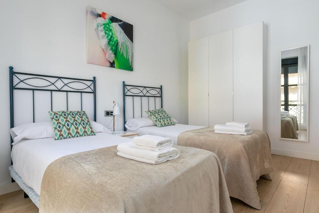 A hotel room with two beds, a large mirror, and a painting on the wall.