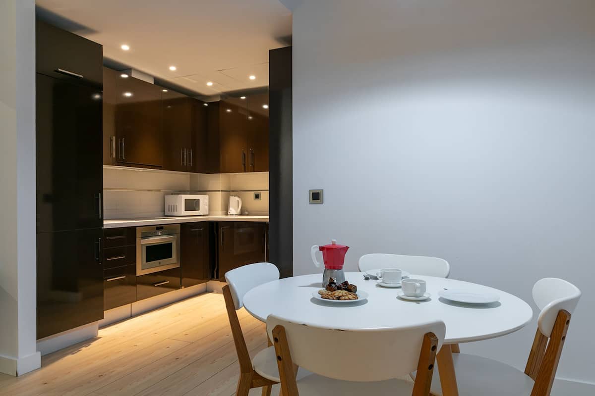 A modern kitchen with dark cabinets, a microwave, and an oven. There is a dining table with chairs and a coffee pot.