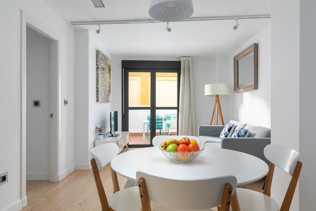 A modern dining area with a round table, white chairs, and a bowl of fruit.
